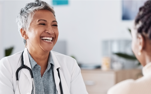 Doctor with short hair and broad smile laughs with patient who we only see from the back.