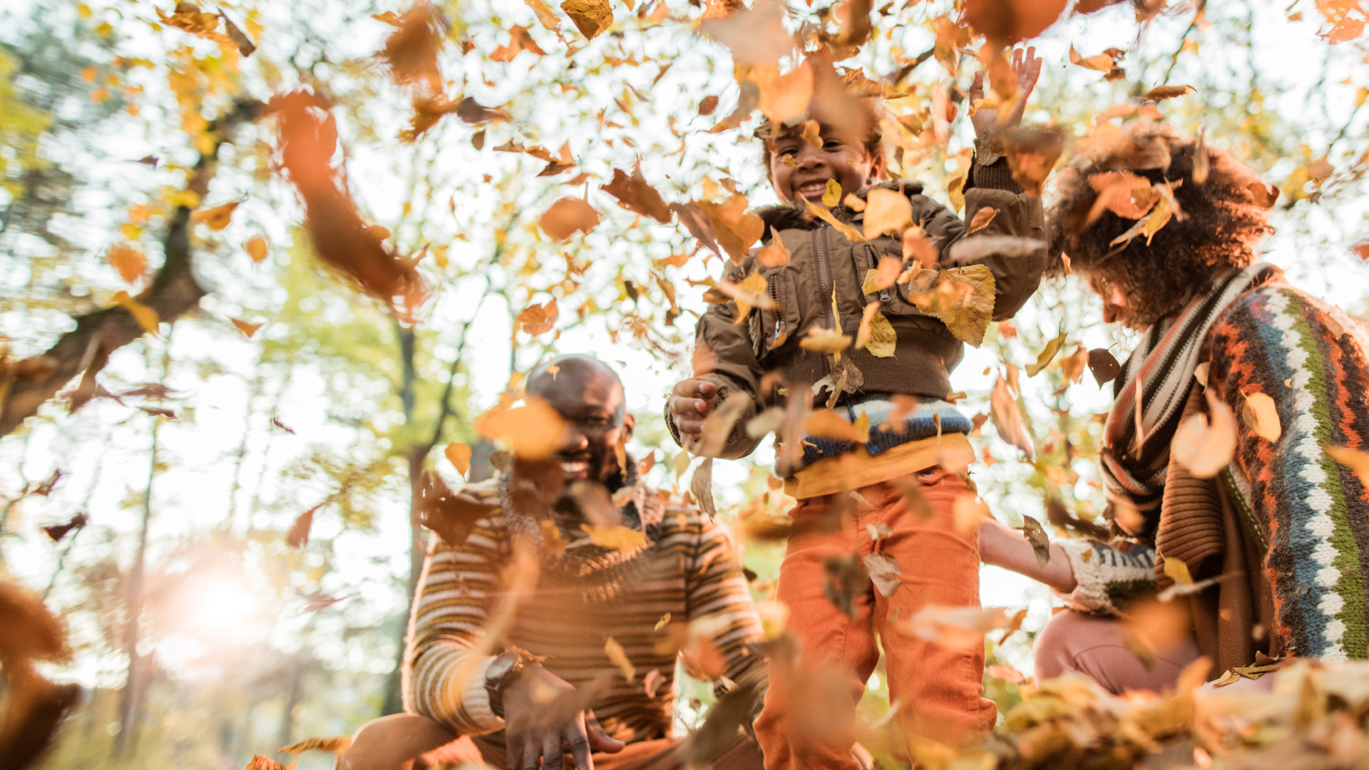 Family in fall leaves. Child throwing fall leaves in the air and laughing.