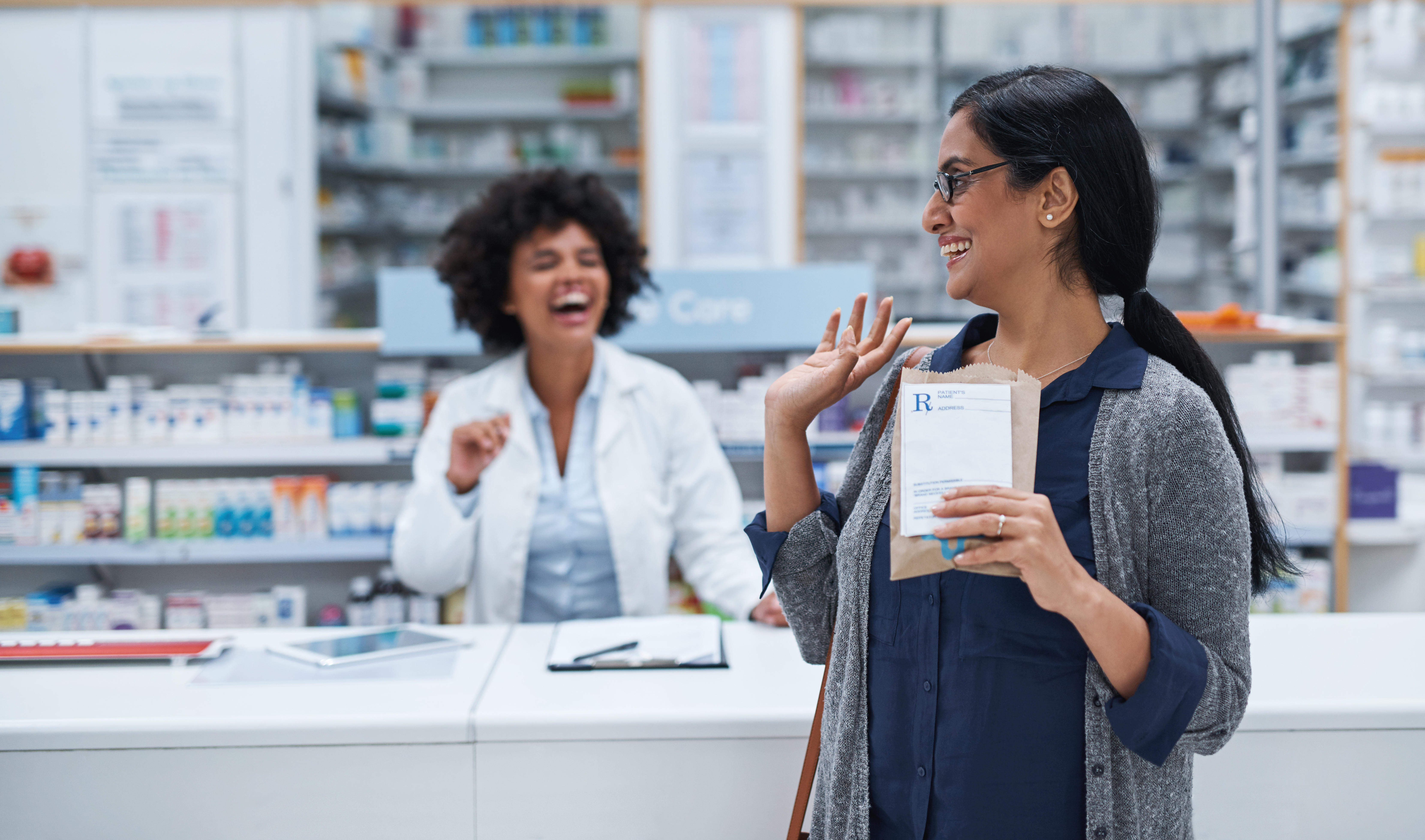 Pharmacist and patient laughing as patient waves goodbye.