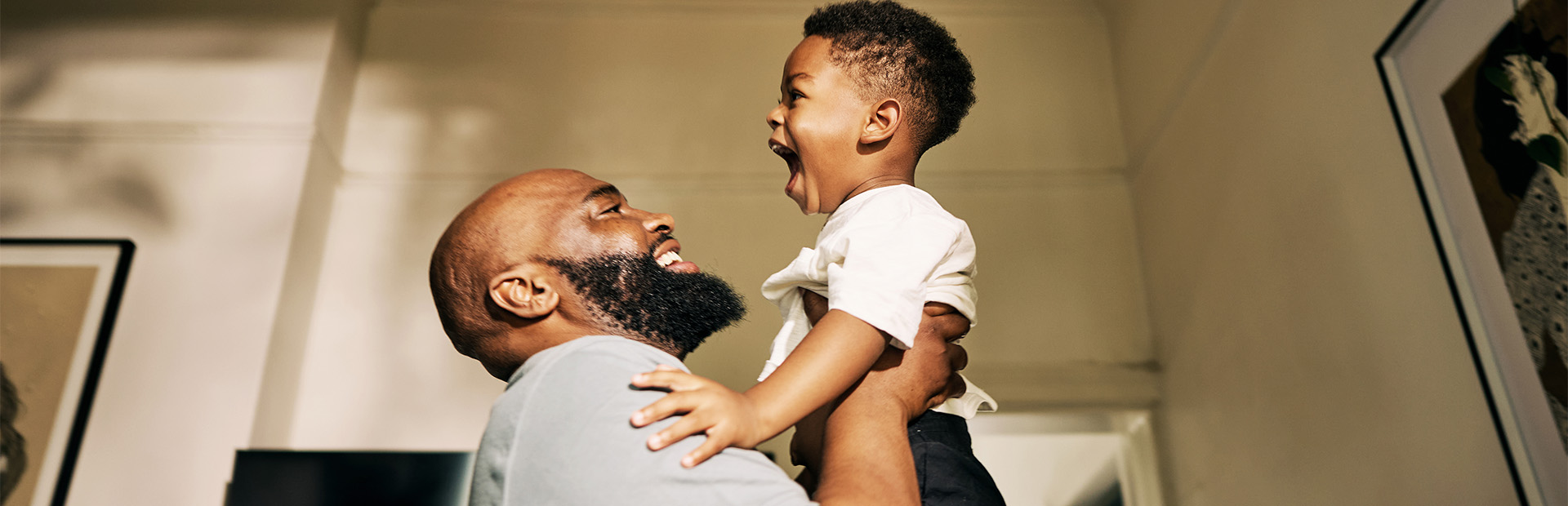 Parent lifting a young child and smiling indoors.