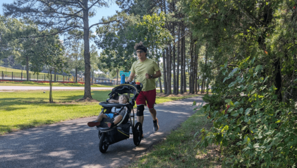 Adam Hertz running outside on a green path and pushing a stroller