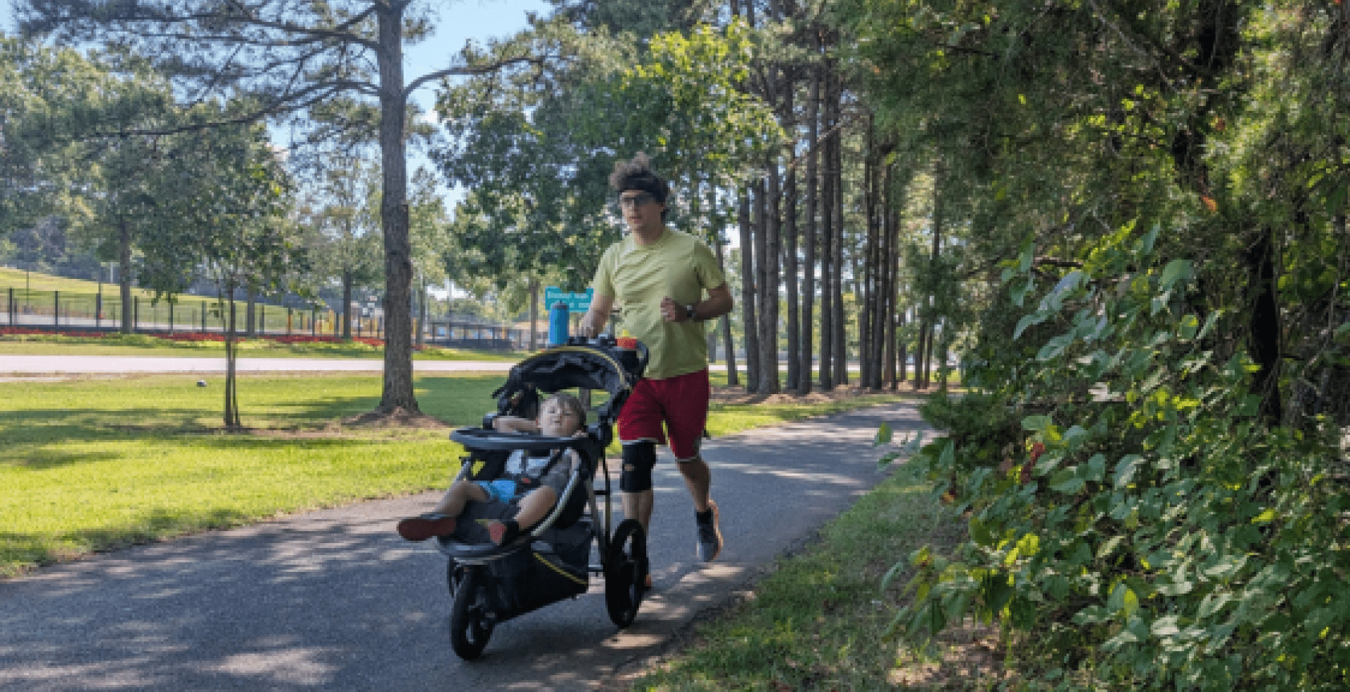 Adam Hertz running outside on a green path and pushing a stroller