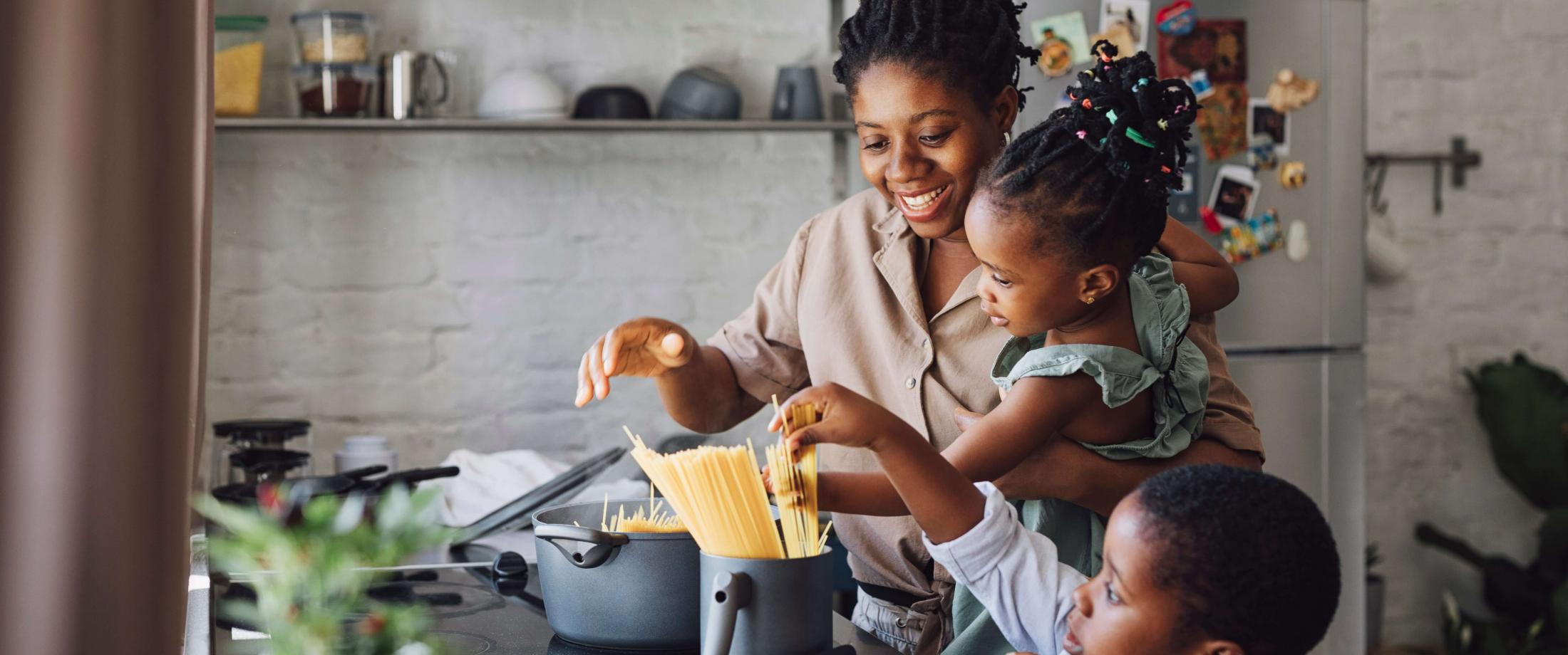Mom cooking pasta along with toddler girl and small boy