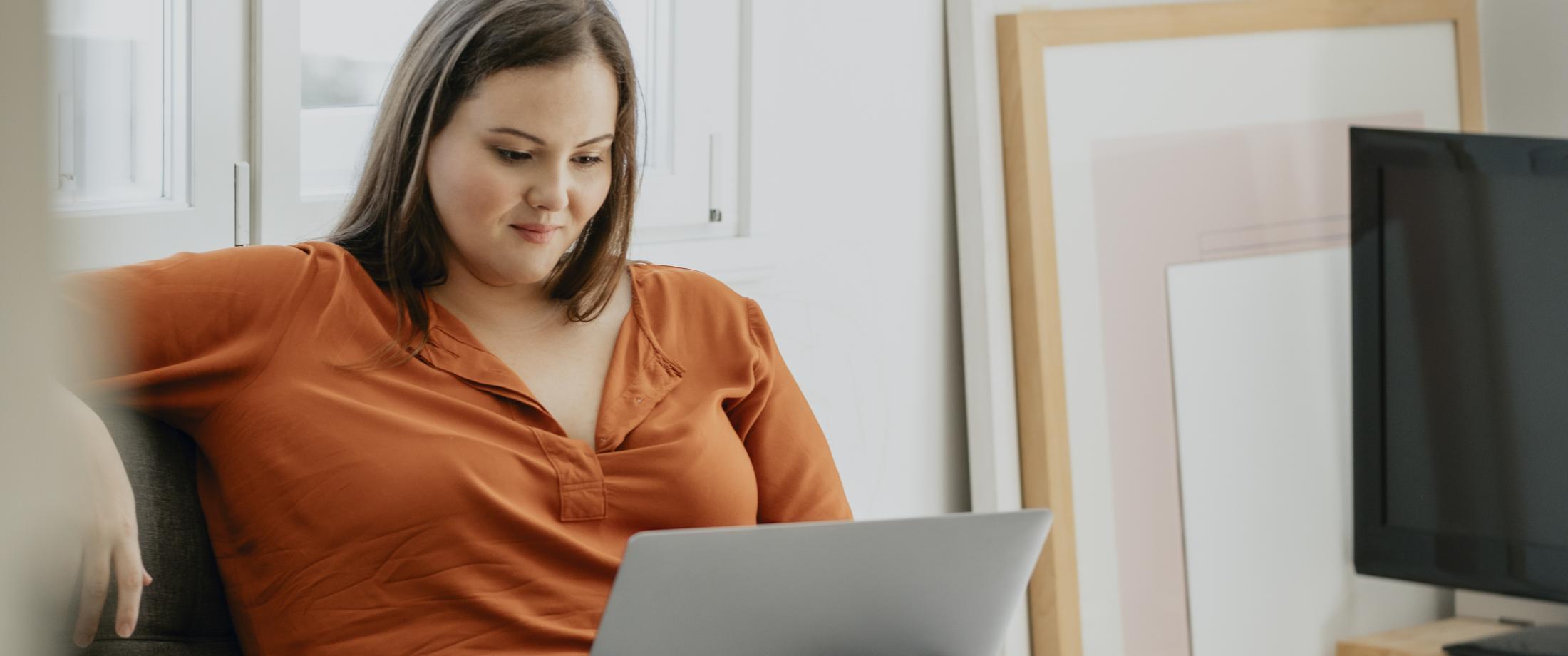 Person at home sitting on comfy chair looking at laptop.