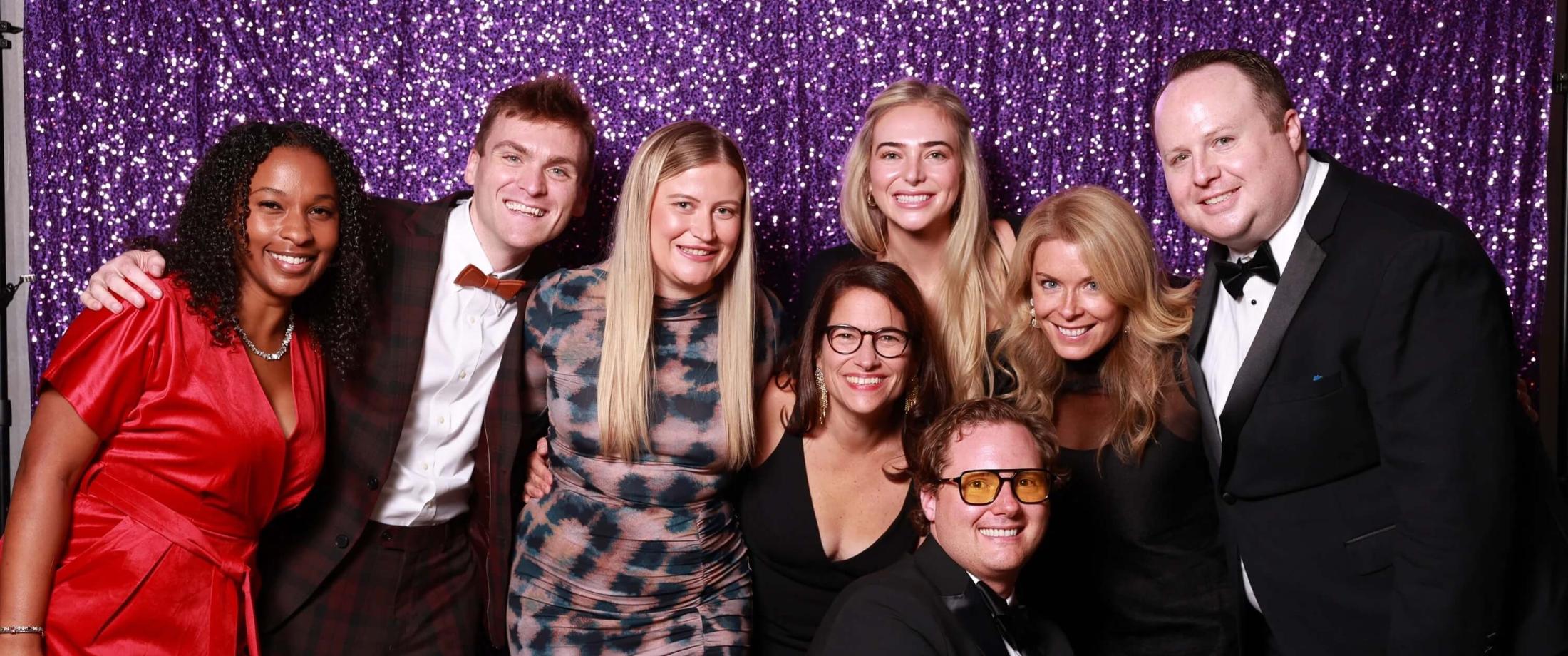 Group wearing black tie posing in front of a glittery purple wall