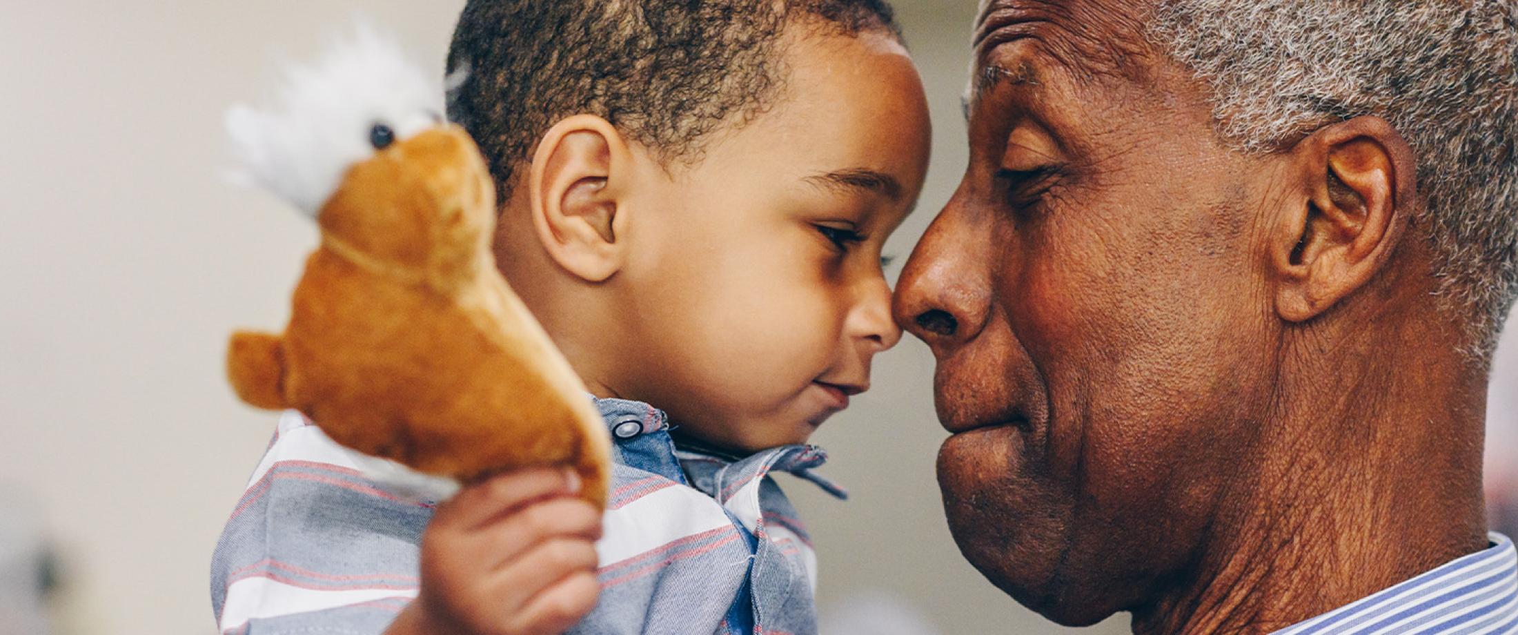 Older adult and young child touching foreheads while holding a stuffed toy.