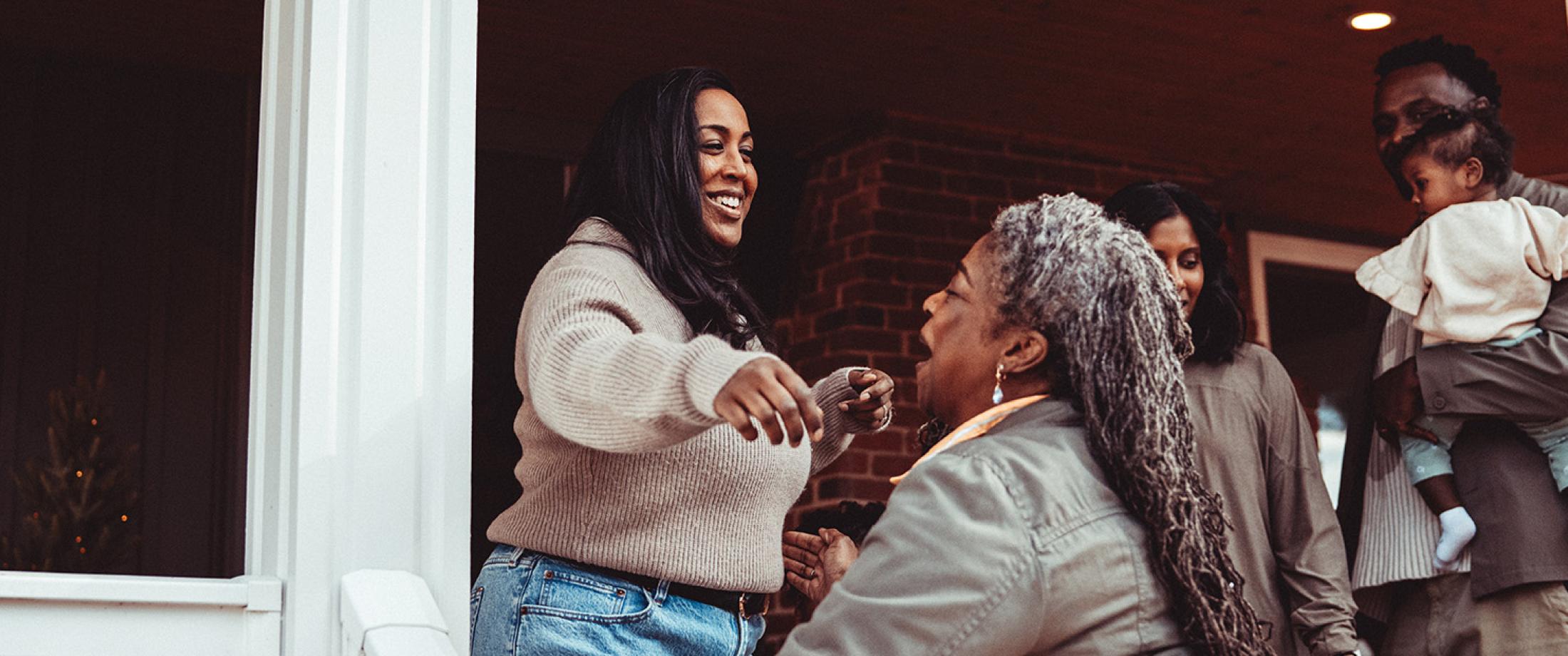 Family members greeting each other with a hug at a front door.