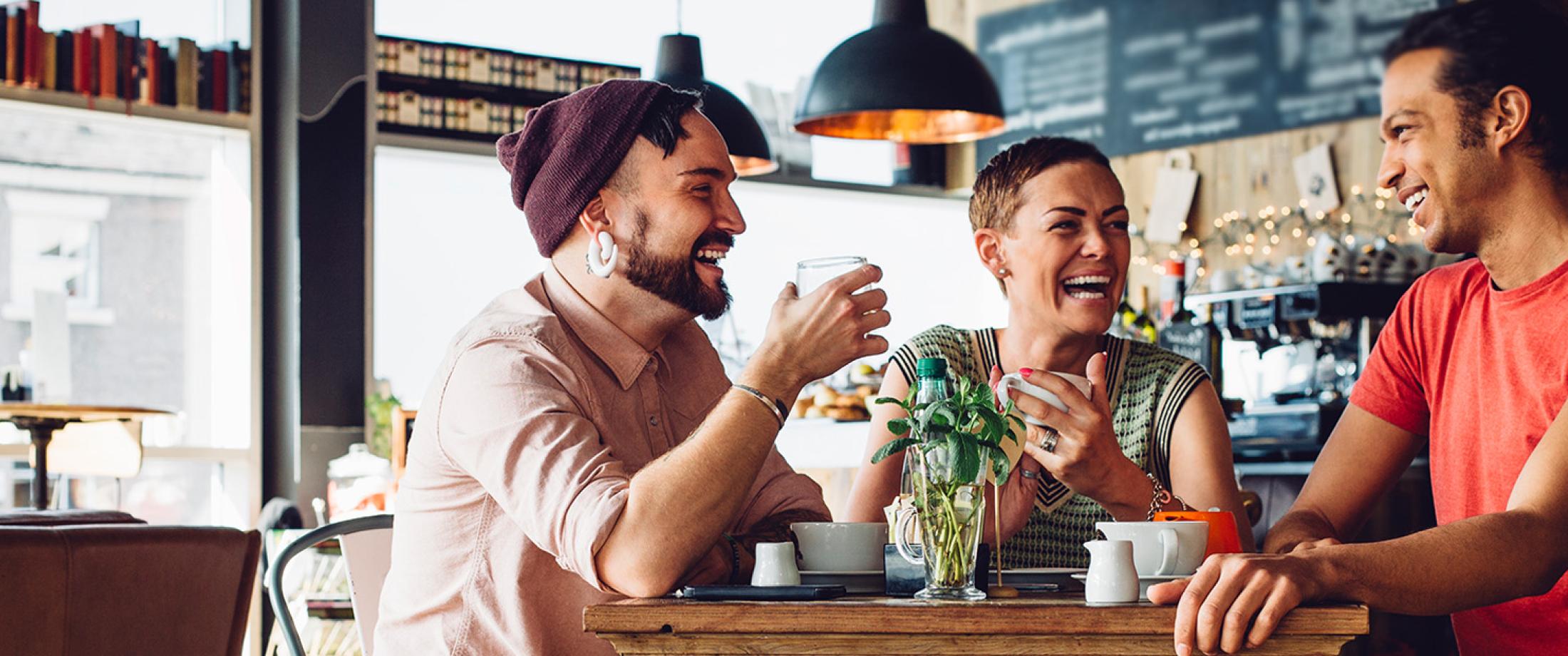 Three adults sitting at a café table and laughing together.