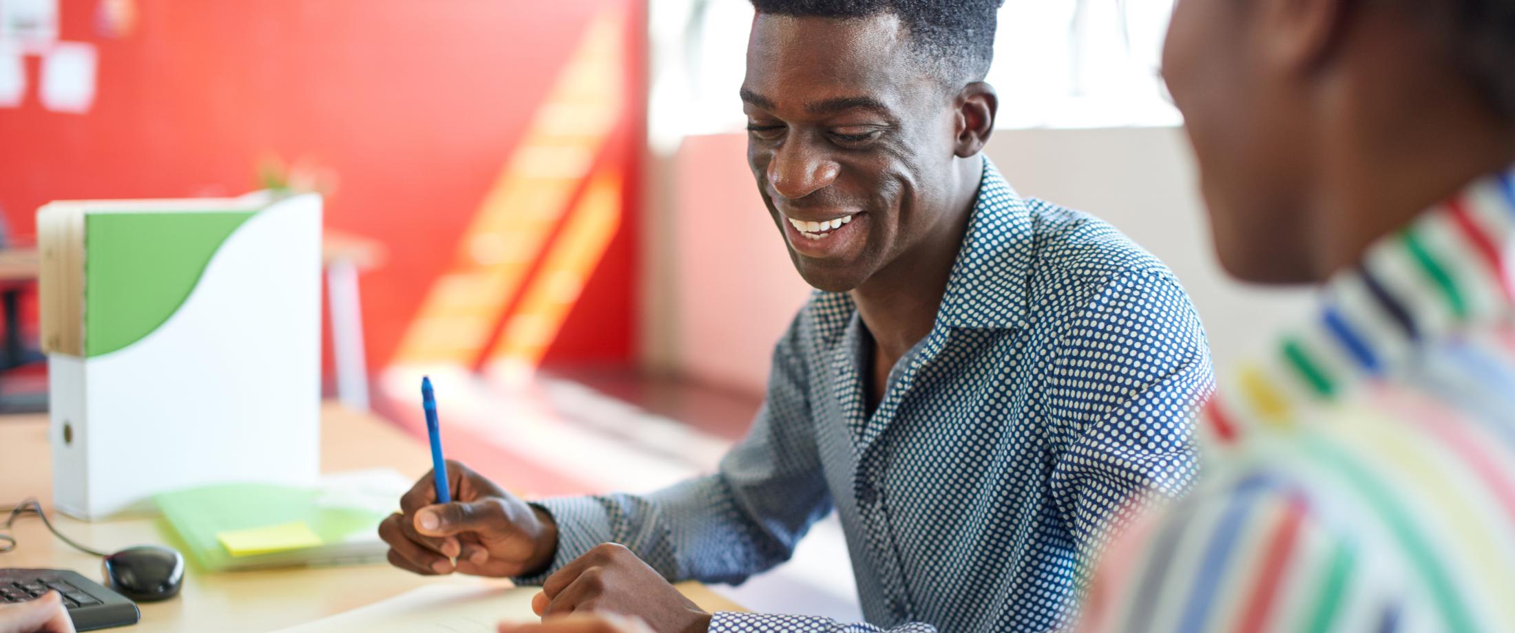 Two people talking while sitting at a desk.