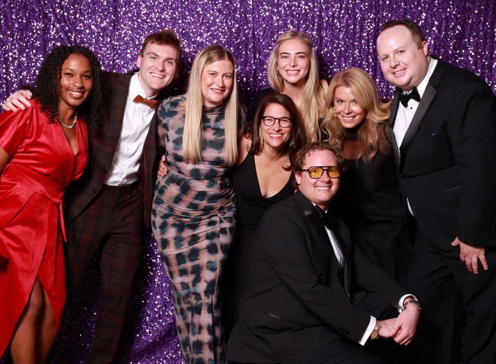 Group wearing black tie posing in front of a glittery purple wall