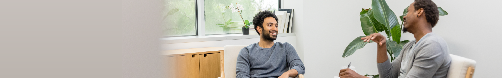 Two individuals sitting in comfortable chairs in an office smiling and talking.