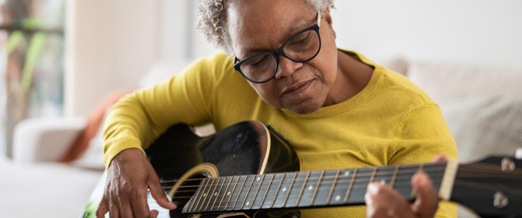Older adult playing an acoustic guitar at home.