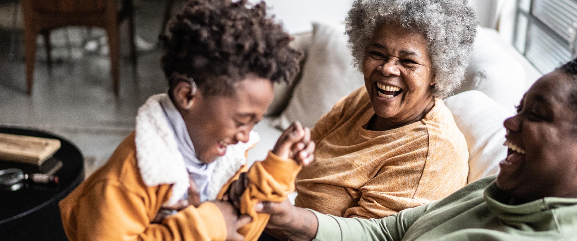 Two adults and a child laughing together on a couch at home.