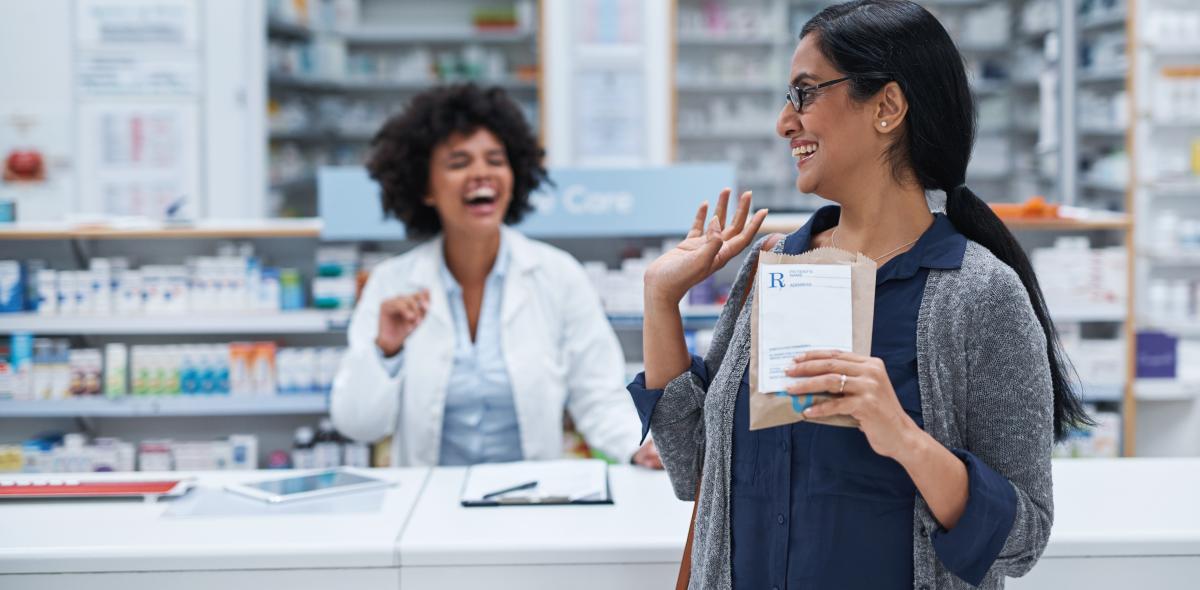 Pharmacist and patient laughing as patient waves goodbye.