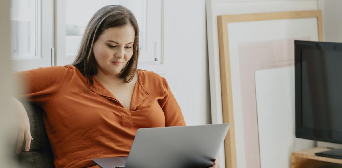 Person at home sitting on comfy chair looking at laptop.