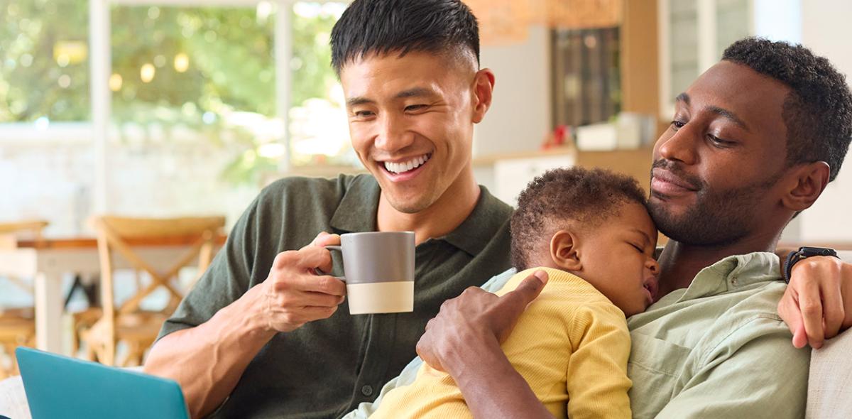 Two parents sitting on a couch while one holds a sleeping baby.