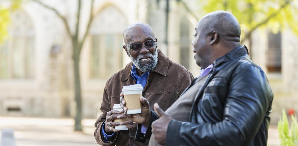 Two older adults enjoying coffee in a park.