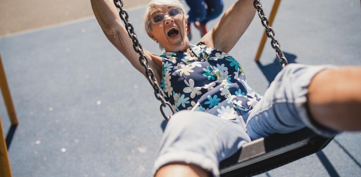 Older person laughing as swinging on playground swing.