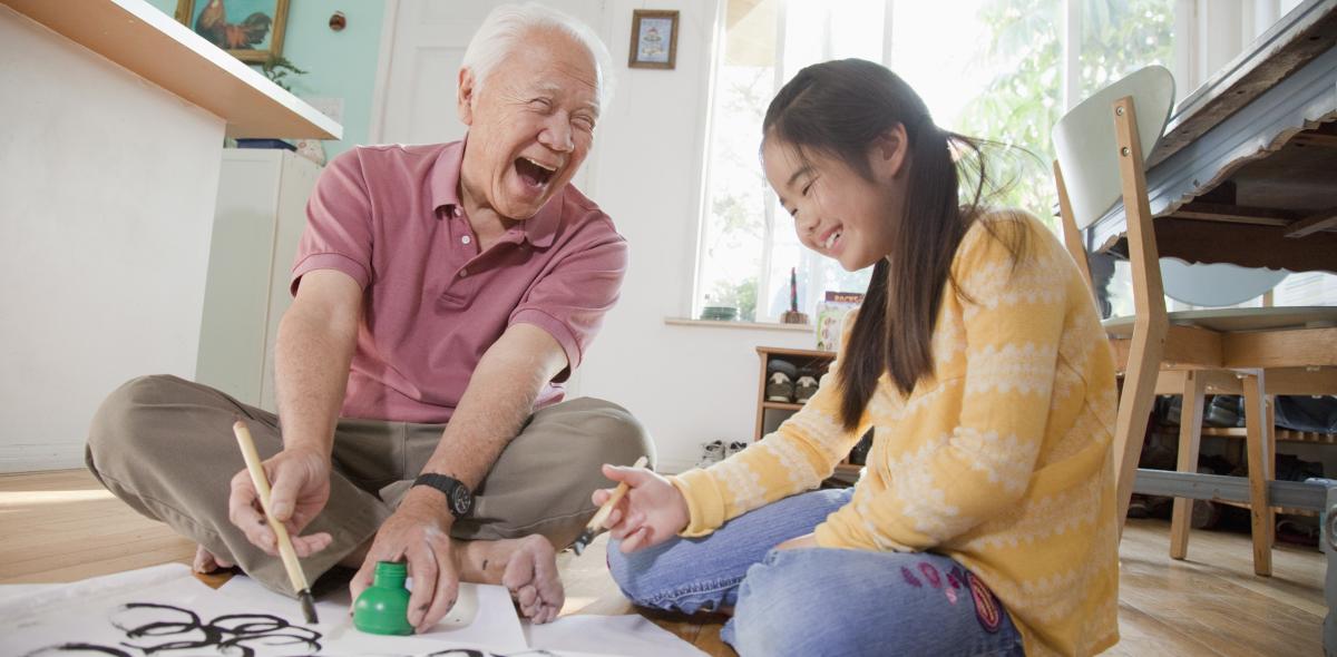 Grandfather and granddaughter laughing while painting.