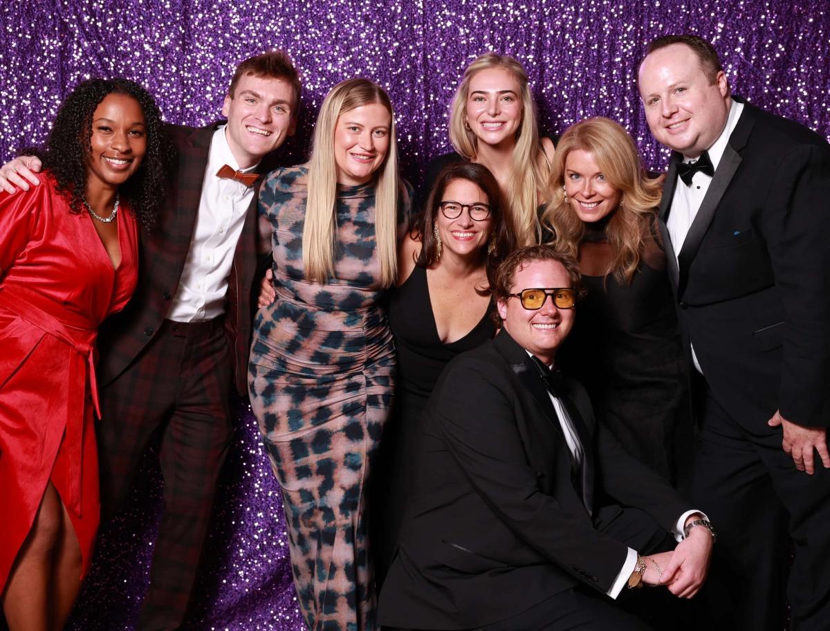 Group wearing black tie posing in front of a glittery purple wall