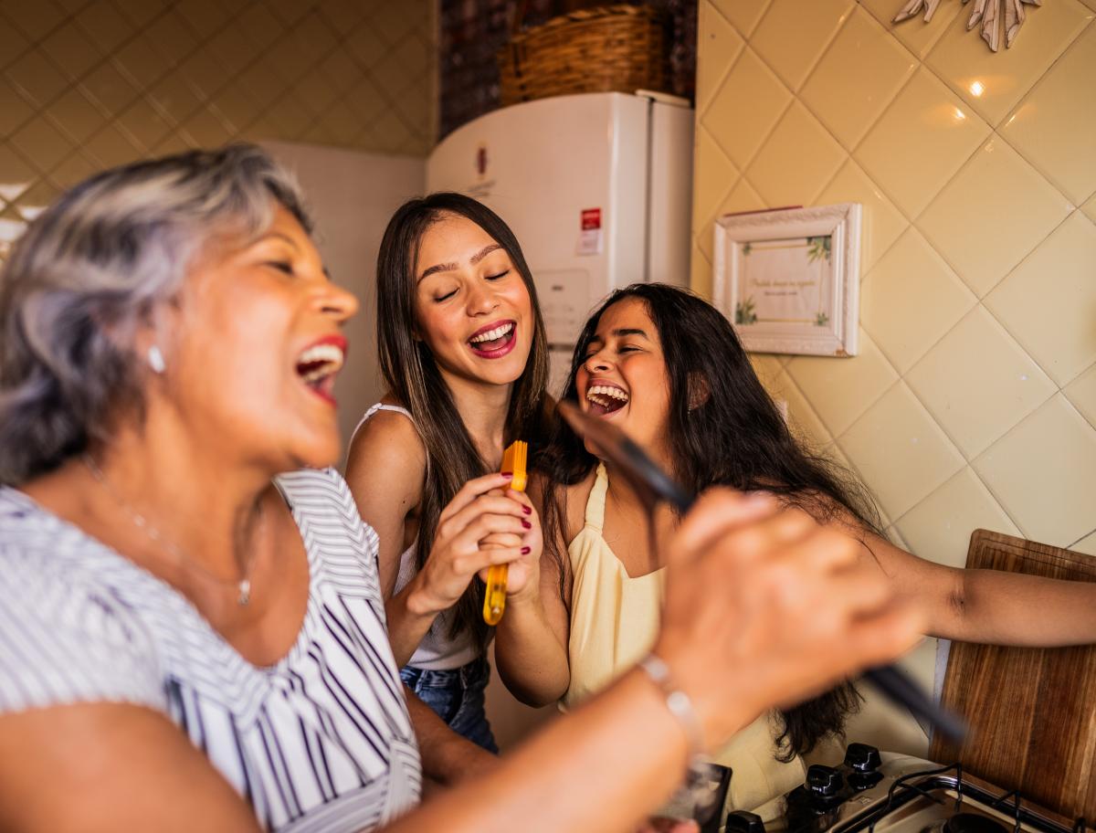 3 generations of women being silly and singing into ladles while cooking.