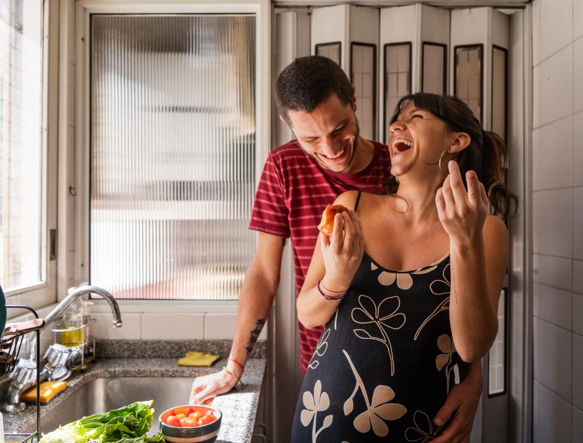 Expecting parents laughing in kitchen.