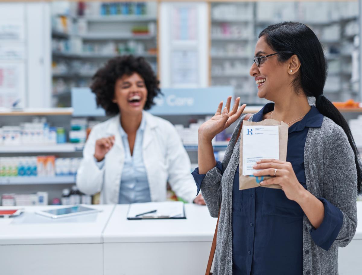Pharmacist and patient laughing as patient waves goodbye.