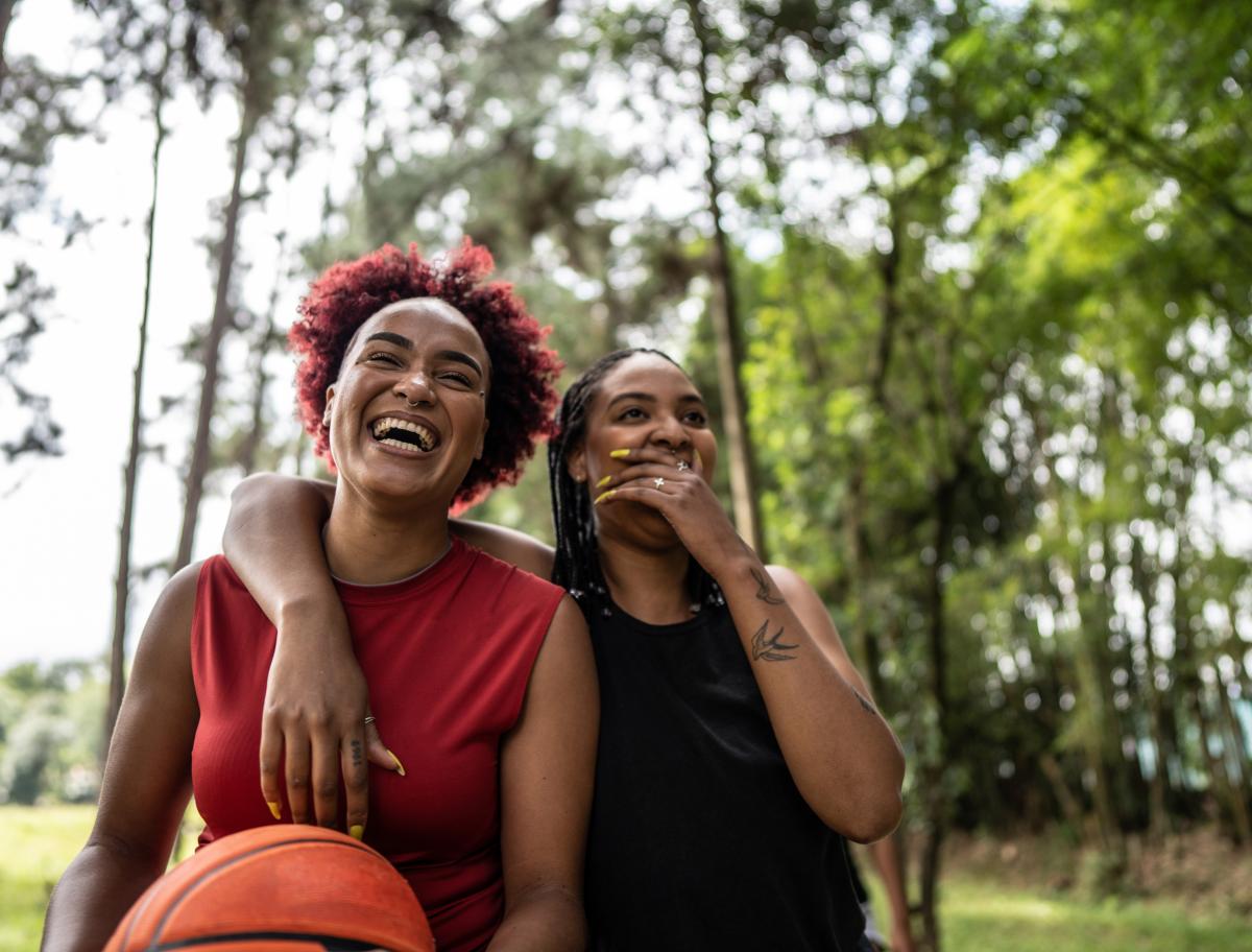 Two women laughing as they walk, one holding a basketball.