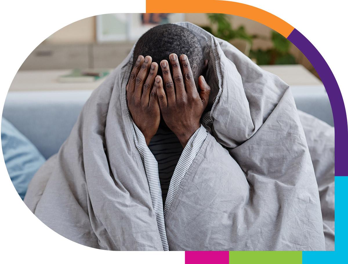 Person draped in comforter with head in hands.