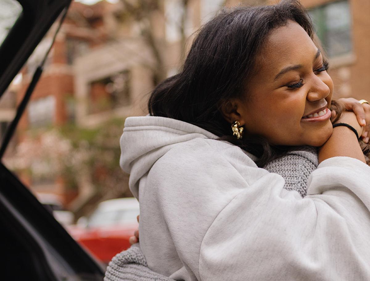 Two women hugging near a parked car on a residential street.