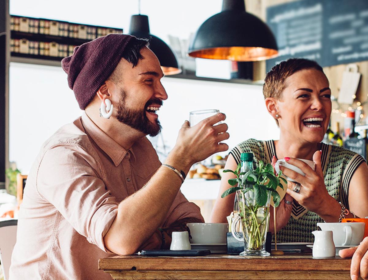 Three adults sitting at a café table and laughing together.