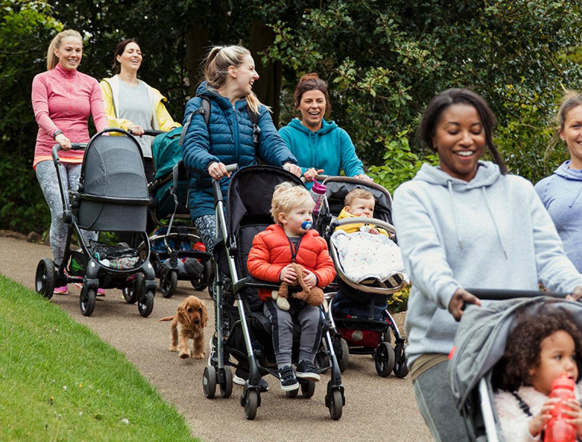 Group of women walking together in a park while pushing strollers.