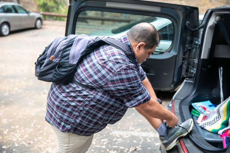 Heavyset man tying his shoe outside his car