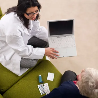 Overhead view of a doctor working on a laptop with a patient on a couch.
