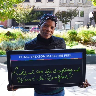 Woman holding sign that says "Chase Brexton make me feel like I can do anything I want to do -- yeah!"