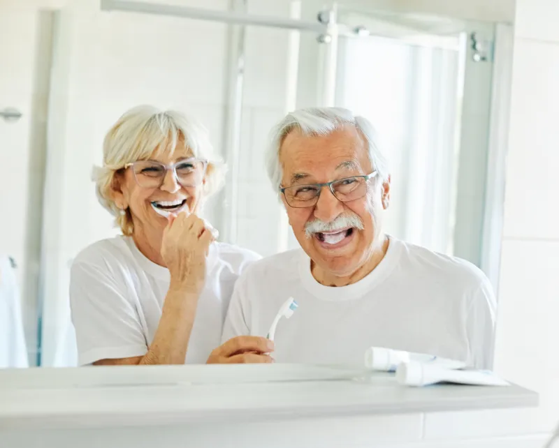 Two older adults brushing teeth.