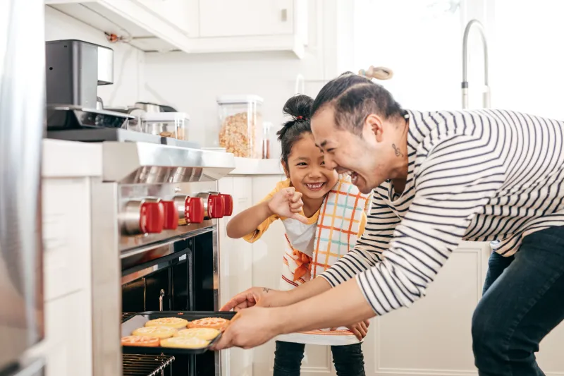 Kid and parent laughing as kid gives thumbs down to parent about cookies coming from the oven.