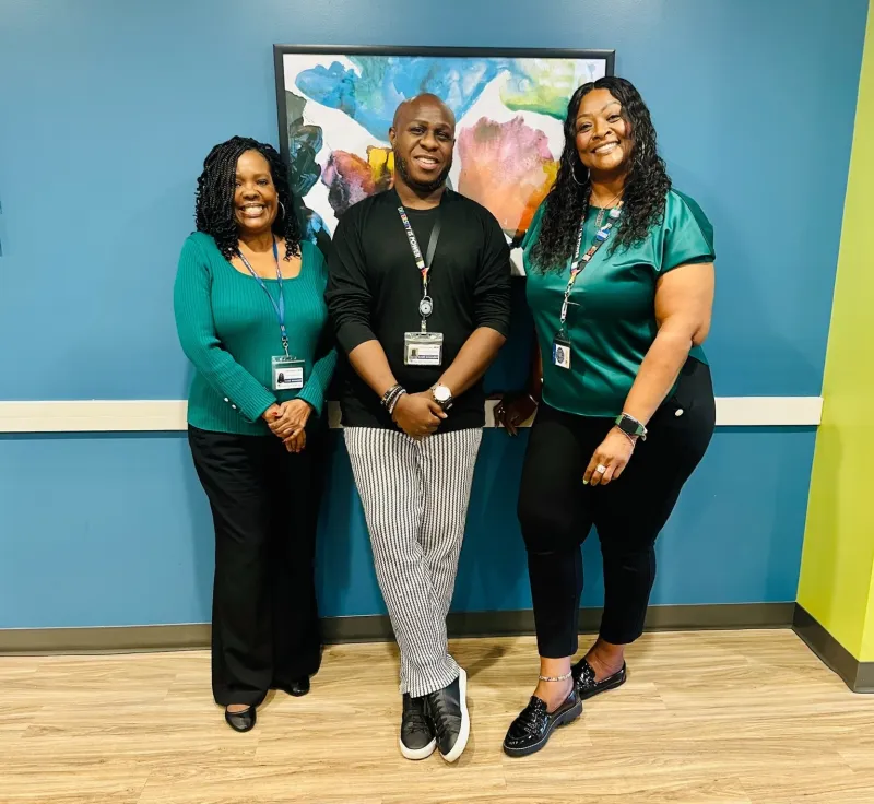 Three people posing together from the Columbia office in front of a teal wall