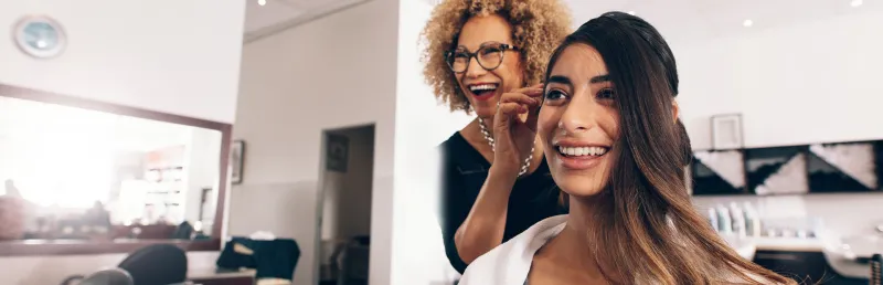 Woman smiling during a hair styling appointment in a professional salon setting.