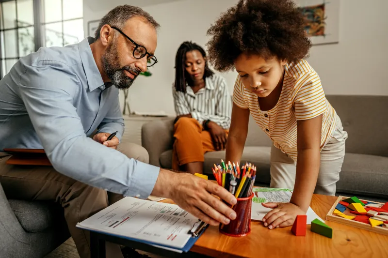 Child doing art therapy with a therapist; guardian sitting in the background.